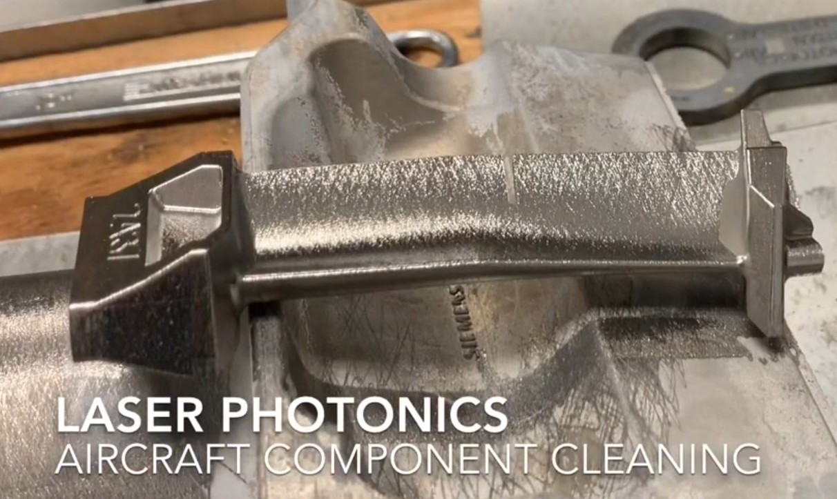 Screenshot from a Laser Photonics aircraft component cleaning video showing a turbine blade with visible mottled surface texture across the airfoil after laser treatment